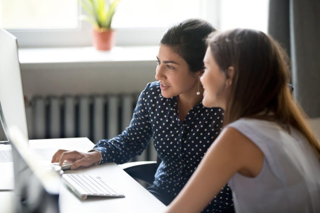 Smiling female colleagues work together at computer